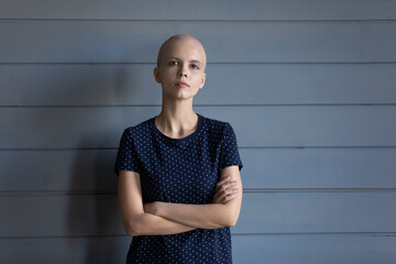 Serious confident cancer survivor head shot portrait. Young hairless woman with arms folded looking...