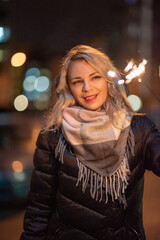 Fototapeta premium Beautiful young blonde girl with sparkler in the night city.