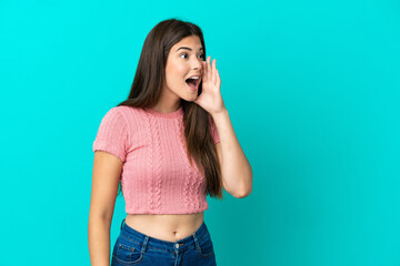 Young Brazilian woman isolated on blue background shouting with mouth wide open to the side