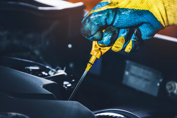Technician hand pulling oil dipstick for checking lubricating oil level of the car engine