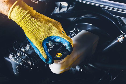 The mechanic is open or close the car's brake fluid reservoir cap to check the brake fluid level