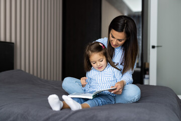 Happy young mother and daughter reading a book together in bed