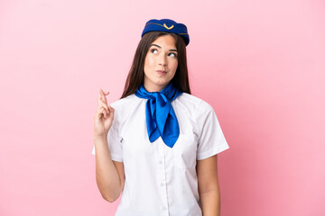 Airplane stewardess Brazilian woman isolated on pink background with fingers crossing and wishing the best