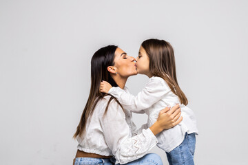 Portrait of little daughter kissing her beautiful happy mother isolated on white background