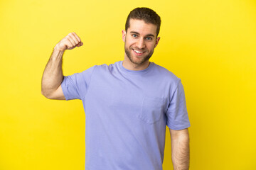 Handsome blonde man over isolated yellow background doing strong gesture