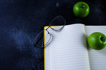 open yellow notebook with glasses and green apples on it
