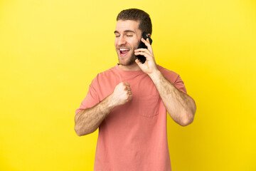 Handsome blonde man using mobile phone over isolated background celebrating a victory