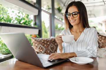 Portrait of gorgeous young woman sitting with open laptop computer in modern coffee shop