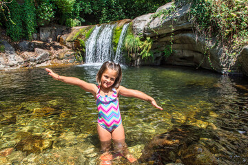 Girl Playing Next To A Rock Inside A River That Has A Beautiful Waterfall. Little Girl In The...