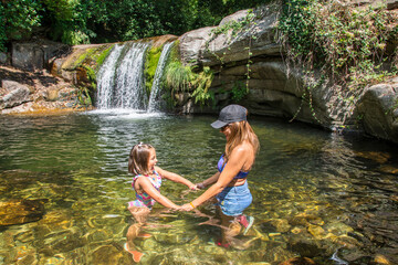 Mother And Daughter Bathing In A River With A Beautiful Waterfall In Nature. Young Woman With A...