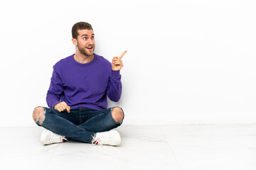Young man sitting on the floor intending to realizes the solution while lifting a finger up
