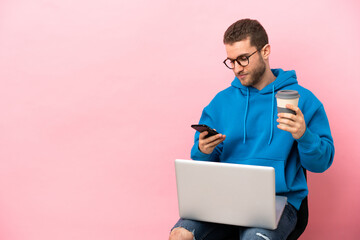 Young man sitting on a chair with laptop holding coffee to take away and a mobile