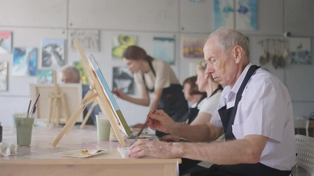 Side view of a happy senior people smiling while drawing as a recreational activity or therapy in paint class together with the group of retired women and men