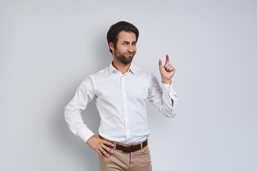 Displeased young man in white shirt looking at camera and gesturing while standing against gray background