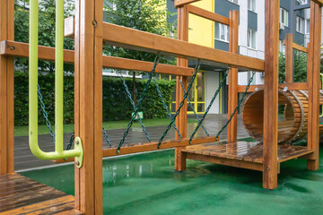 A courtyard of high-rise buildings with a modern and large playground made of wood and plastic on a rainy summer day without people. Empty outdoor playground. A place for children's games and sports.