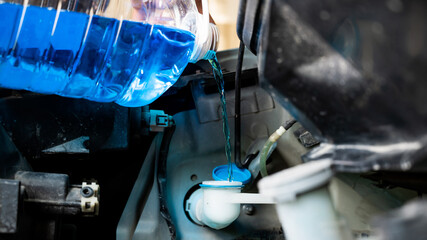 Auto mechanic pours windshield washer fluid into the car.