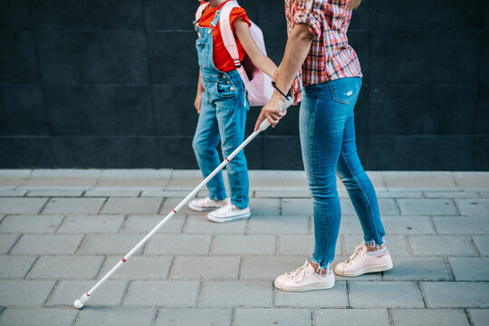 Young blind mother walking with her little daughter on city street.