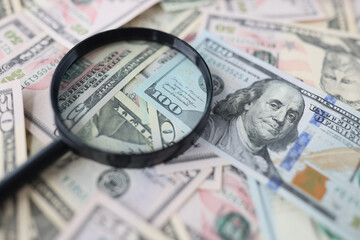 One hundred dollar bills and magnifying glass lie on table closeup