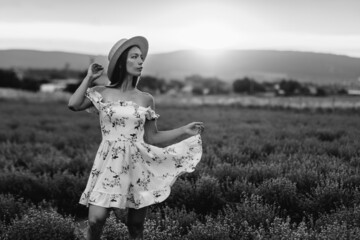 A young beautiful girl in a delicate dress and hat walks through a beautiful field of lavender and...