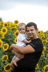 Fototapeta premium brunette male young dad with cute child blonde son on a field of sunflowers.
