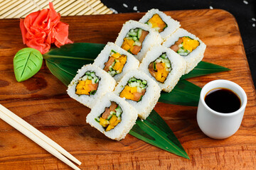 vegan sushi roll with vegetables on a wooden board on a background of ginger and soy sauce on a dark background