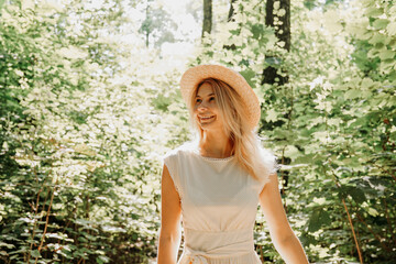 Beautiful young woman in a straw hat and white dress in a green park or forest on a summer day