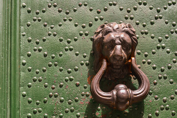 Close-up of a studded green door with a lion head knocker in the historic centre of Genoa, Liguria, Italy