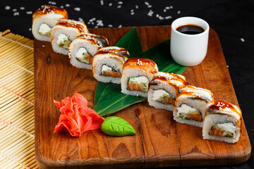 sushi roll with eel and salmon on a wooden board on a background of ginger, wasabi and soy sauce on a dark background
