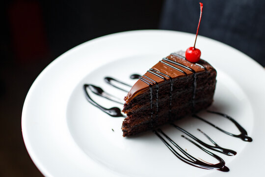 a piece of chocolate cake with a cherry on a white plate on a dark background