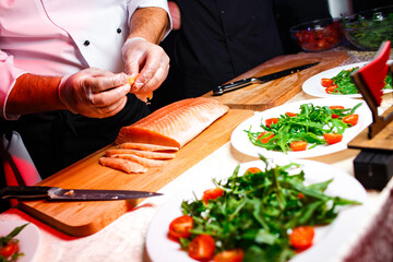 the chef cuts the salmon fillet and prepares a salad from it on a dark background