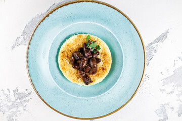 traditional couscous in a round form with chicken hearts in a blue plate on a white background. top view..
