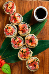 tempura sushi roll with salmon and tuna on a wooden stand with ginger, wasabi and soy sauce close-up