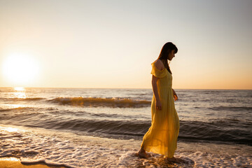 Fototapeta na wymiar Young woman walks along seashore at sunset. Nature, relax, lifestyle concept.