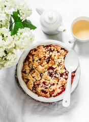 Raspberry peaches crumble in a baking dish and green tea on a light background, top view. Summer dessert