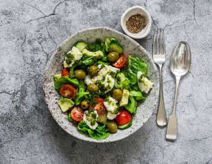 Fresh vegetable salad with tomatoes, avocado, lettuce, cucumbers, borata and pesto sauce dressing on a gray background, top view
