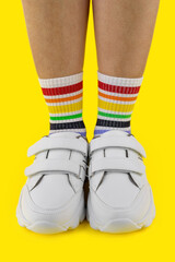 women's legs in multi-colored socks in the white sneakers on colored background, close-up, vertical image