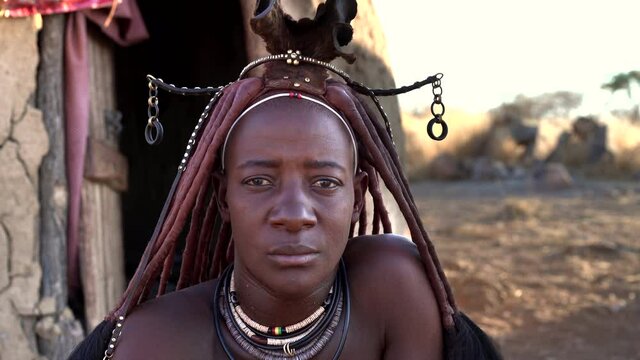 Married Himba woman looking at camera and wearing traditional jewelry and Erembe headpiece at her village near Kamanjab in Namibia, Africa.