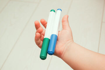 A child's hand holds two felt-tip pens.