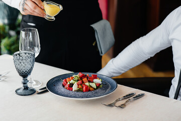 A waiter pours sauce over a fresh salad of vegetables and tuna in close-up. Healthy food.