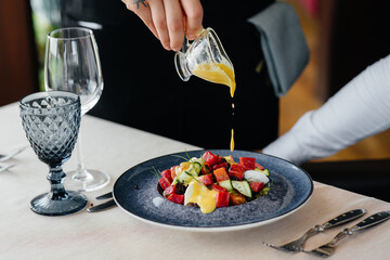 A waiter pours sauce over a fresh salad of vegetables and tuna in close-up. Healthy food.