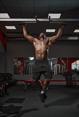 Fototapeta na wymiar Handsome muscular athletic african american man doing chin-ups or pull ups exercising on training in gym