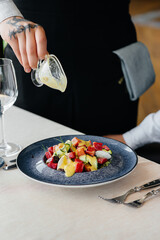 A waiter pours sauce over a fresh salad of vegetables and tuna in close-up. Healthy food.