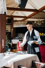 A young male waiter in a stylish uniform is engaged in serving the table in a beautiful gourmet restaurant. Restaurant activity, of the highest level.