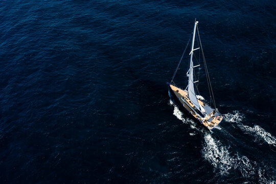 View from above, stunning aerial view of a sailboat sailing on a blue water at sunset. Costa Smeralda, Sardinia, Italy.
