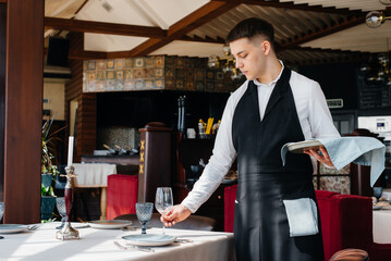 A young male waiter in a stylish uniform is engaged in serving the table in a beautiful gourmet restaurant. Restaurant activity, of the highest level.