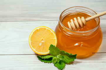 fresh honey in a transparent jar on a wooden background and lemon with mint, healthy lifestyle. High quality photo