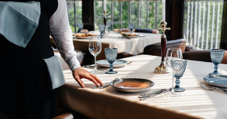 A young waiter in a stylish uniform is engaged in serving the table in a beautiful gourmet restaurant close-up. Restaurant activity, of the highest level.
