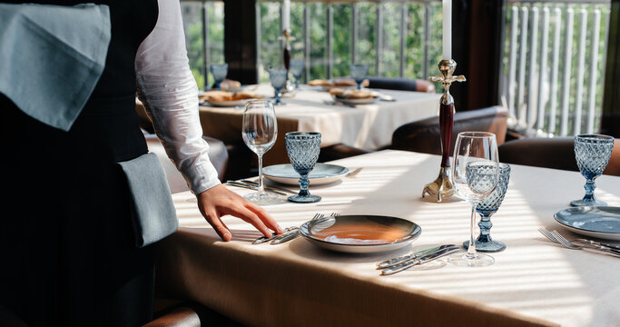 A young waiter in a stylish uniform is engaged in serving the table in a beautiful gourmet restaurant close-up. Restaurant activity, of the highest level.