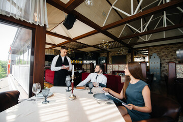 Fototapeta premium A stylish waiter serves a young couple who came on a date in a gourmet restaurant. Customer service in the catering.