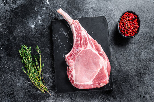 Raw fresh tomahawk pork chop steak on a marble board. Black background. Top view